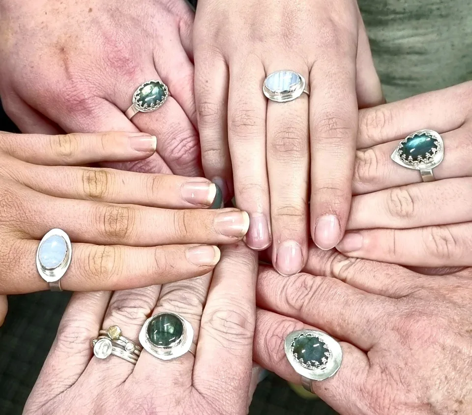 Six hands together, each wearing hand-made silver rings set with green and blue stones