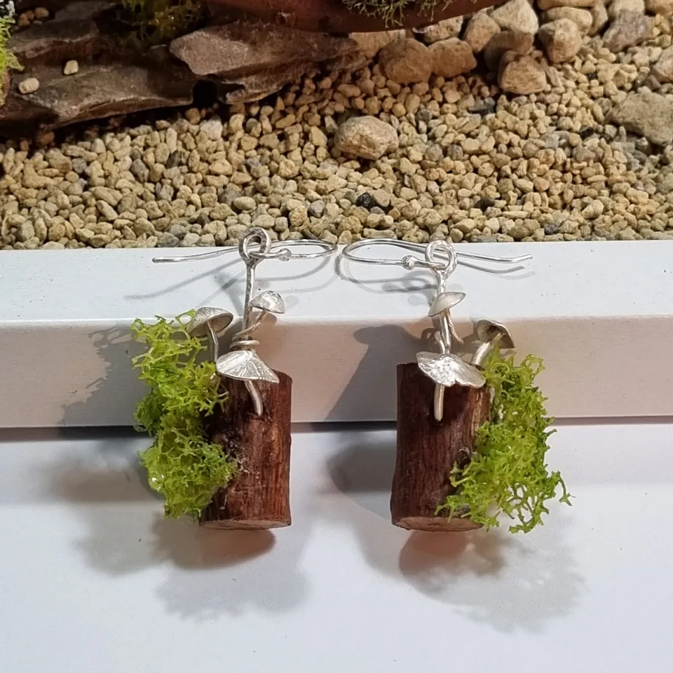 A pair of silver drop earrings standing on moss-topped wooden blocks