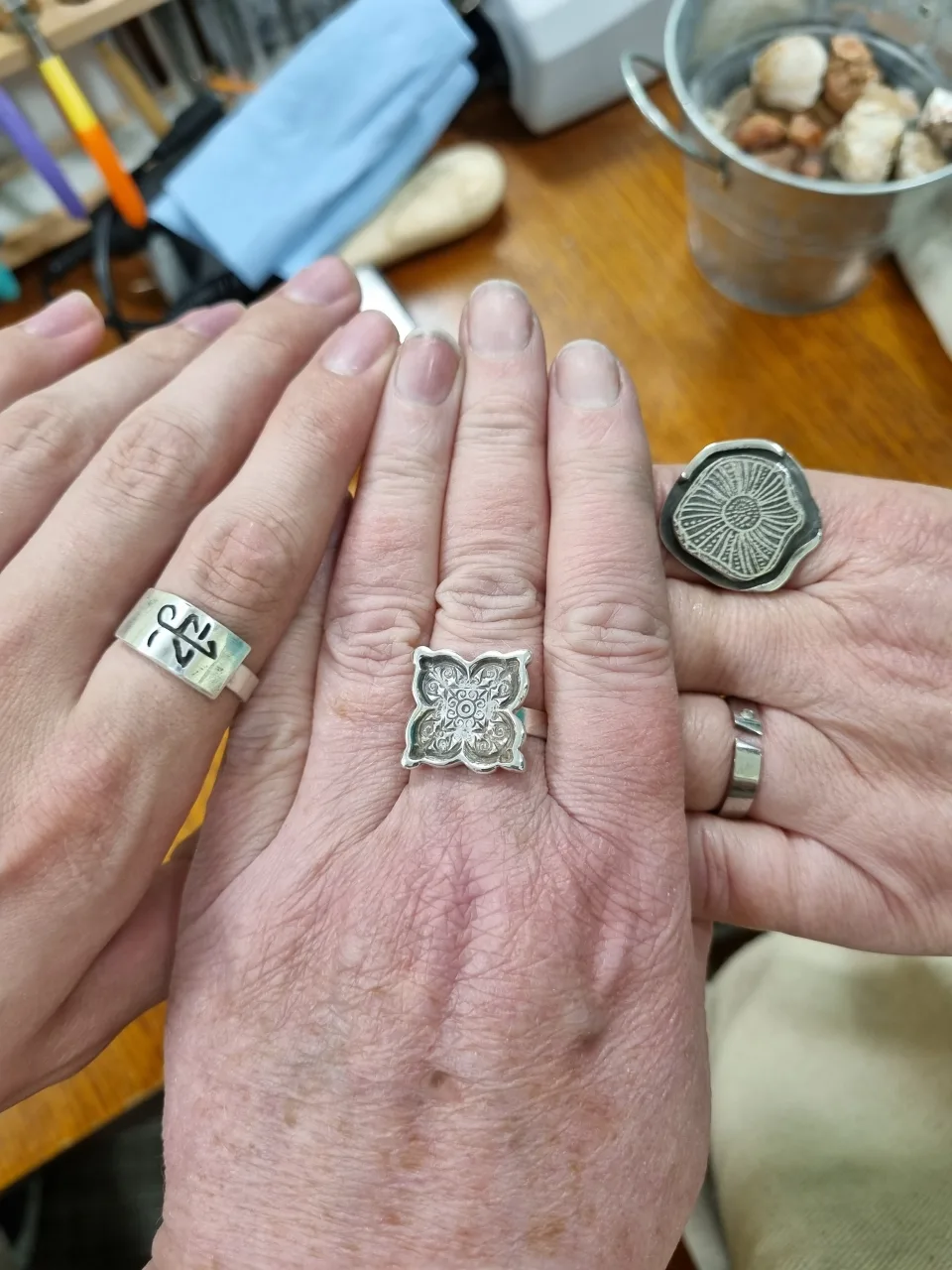 Hands wearing four hand-made silver rings, one carved with a flower