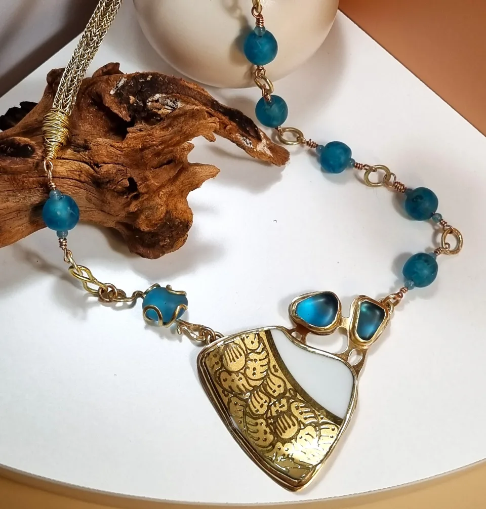 A necklace of teal stones with a large engraved pendant, displayed on a stand